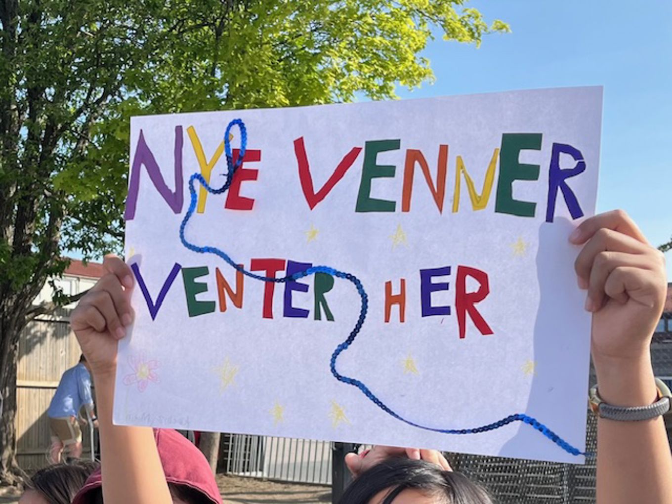 en gruppe mennesker som holder et skilt hvor det står "nye venner venter her"